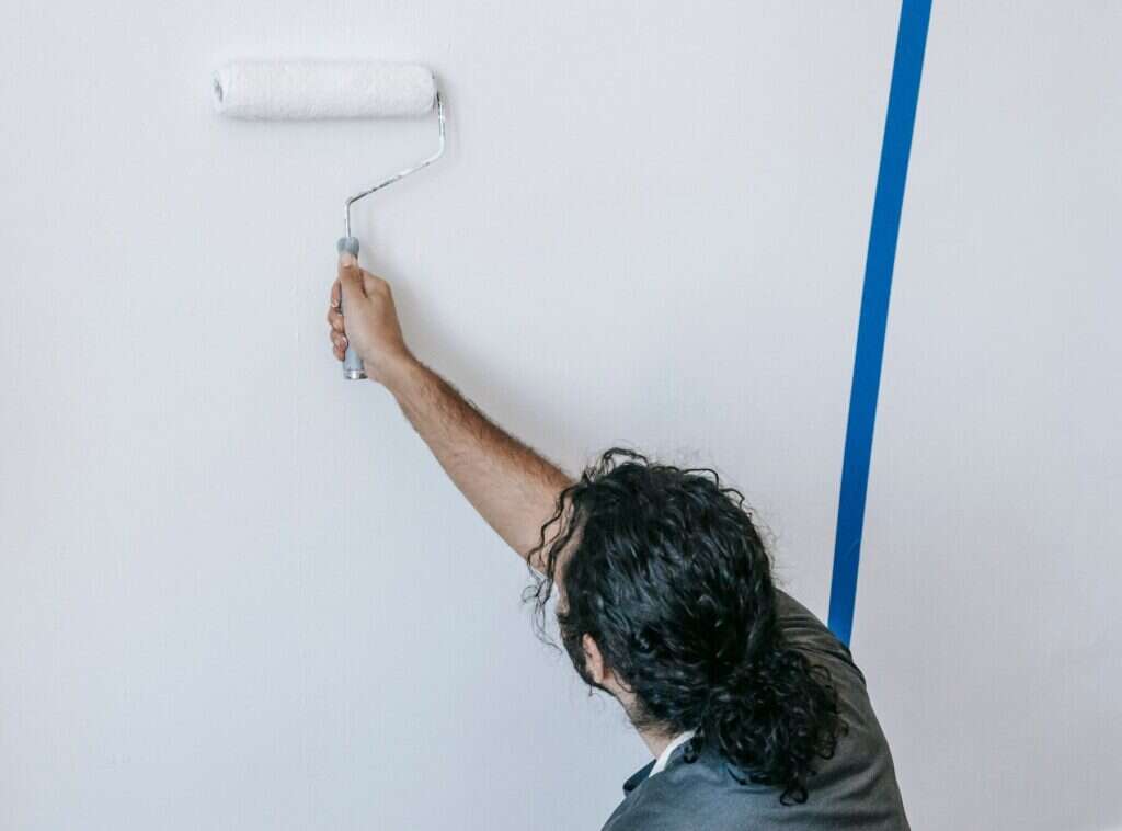 Pintor aplicando pintura con rodillo en la pared de un piso vacio